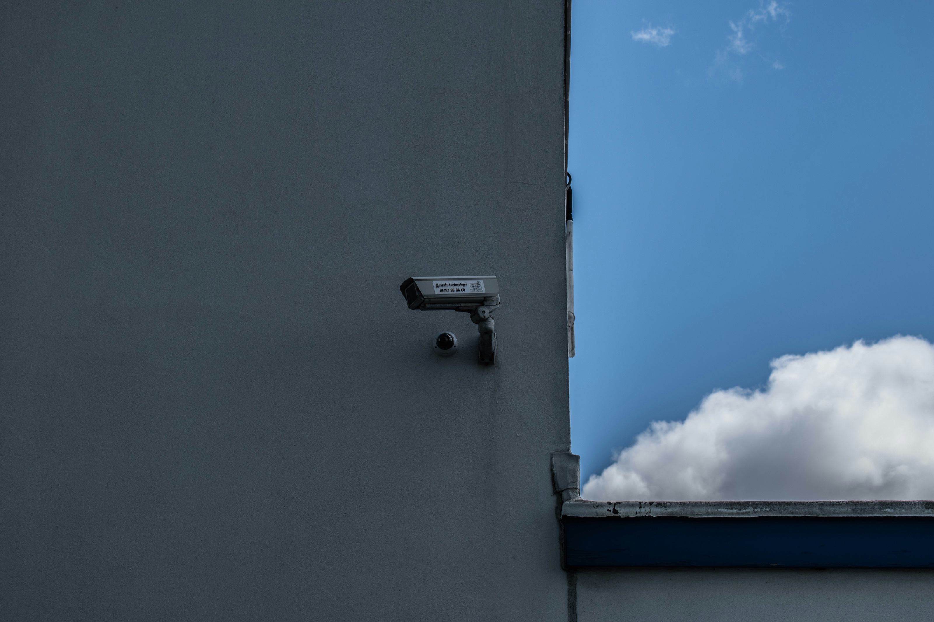 Surveillance camera on a building edge against blue sky and cloud