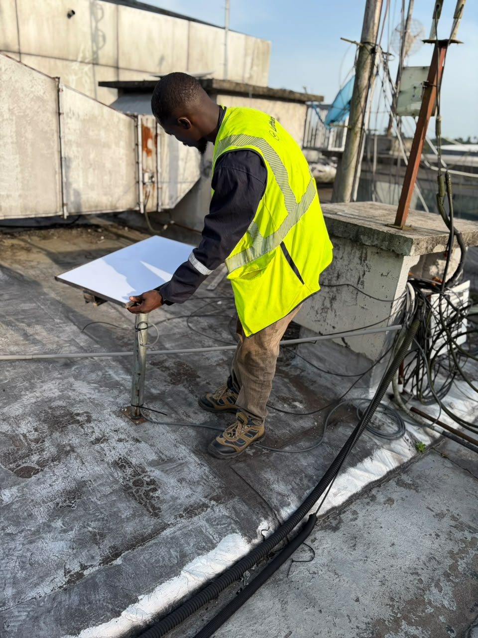 Namiks technician in a hi-vis vest mounting a satellite uplink dish on a Port Harcourt rooftop
